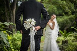 Portrait of a groom hiding a flower bouquet behind his back to surprise bride photo