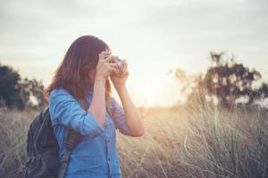Young hipster woman backpacker with a vintage camera standing in a field photo