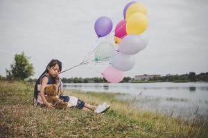 Niña con un oso de peluche y globos en el campo de la pradera foto