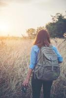 Young hipster woman backpacker with a vintage camera standing in a field photo