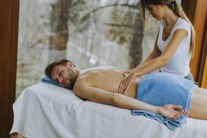 Handsome young man lying and having back massage in spa salon during winter season photo