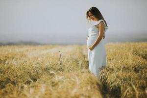 Young pregnant woman in white dress relaxing outside in nature photo