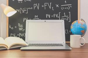 A laptop sitting on a desk with a globe, coffee cup and book photo