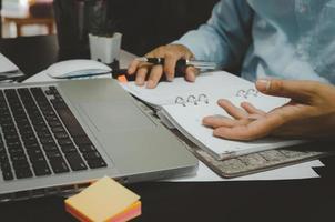 A businessman taking notes in a marketing strategy planner and statistics looking at computer data photo