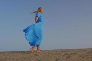 Mujer descalza caminando en la arena con un vestido azul foto