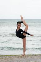 Girl gymnast in black on a beach