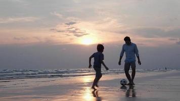 Silhouetten der Familie, die glücklich Fußball am Strand spielt