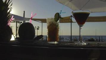 Multiple cocktails on a bar with sun setting into the sea in the background video