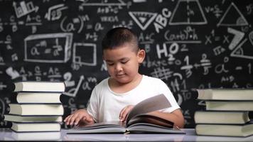 Asian school boy sitting at desk and reading a book video