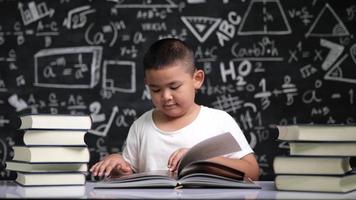 ragazzo asiatico della scuola che si siede allo scrittorio e che legge un libro video