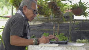 Hombre mayor asiático usando la computadora portátil y escribiendo en el bloc de notas