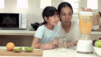 Frau und kleines Mädchen machen orange Smoothie mit elektrischen Mixer. video