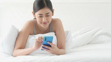 asiatisches Mädchen, das auf dem Bett liegt und auf einem Smartphone tippt video