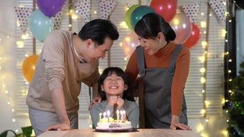Aziatische familie blaast kaarsjes op een verjaardagstaart thuis