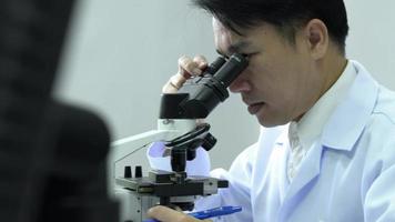 asiatischer Wissenschaftler, der auf einem Mikroskop in einem Wissenschaftslabor schaut