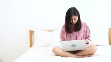 Femme asiatique assise sur le lit à l'aide d'un ordinateur portable video