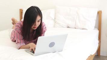 asiatische junge Frau, die auf Bett mit einem Laptop liegt und lacht video