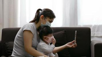 Mutter und Tochter tragen eine Maske und unterhalten sich bei einem Videoanruf