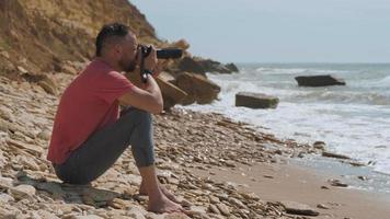 homme assis au bord de la mer avec un appareil photo video