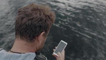 l'homme est assis sur une jetée et regarde le téléphone video