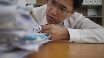 Overworked businessman looking at a stack of paper documents in hid office video