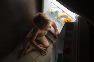 Little boy sitting near an open fridge at night photo