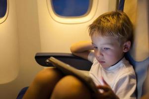 niño sentado en un avión usando una tableta foto