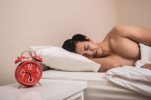 Man sleeps in bed with red alarm clock