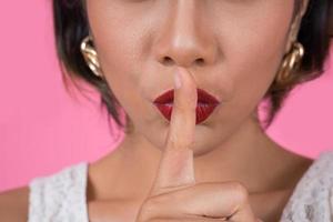 Beautiful Asian woman with red lips showing hush silence sign photo