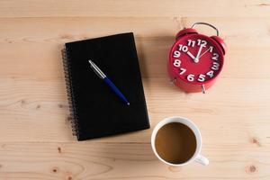 Red alarm clock with notepad and coffee on wooden table photo