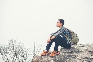 Young hipster hiker with backpack sitting on top of the mountain photo