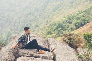 Excursionista joven inconformista con mochila sentado en la cima de la montaña foto