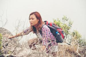 Young Asian woman hiker climbing rock on mountain peak photo