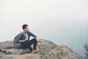 Excursionista joven inconformista con mochila sentado en la cima de la montaña foto