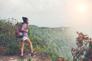 Caminante con mochila de pie en la cima de una montaña y disfrutando de la vista de la naturaleza