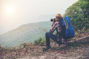 Parte trasera del joven viajero hombre con mochila de pie en la montaña y tomar una foto