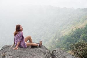 Young hiker with backpack sits on the edge of the cliff