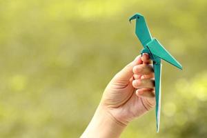 Hand holding blue origami bird with blurred nature background photo