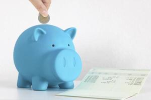 Hand inserting coin into blue piggy bank photo