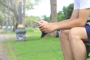 Young man sitting on park bench cell using phone in public park photo