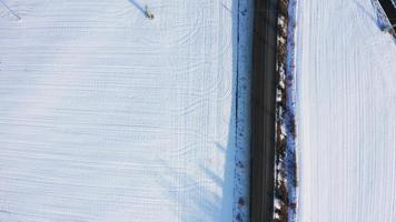 vista aérea de cima para baixo de uma rodovia e um campo de neve branca em 4k video