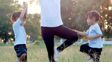 Family doing yoga. Two little girls and mother standing, keeping balance in a park. video