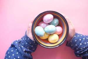 Child  holding a bowl of easter eggs on pink background photo