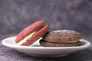 Chocolate and red vanilla cookies on plate against black background photo