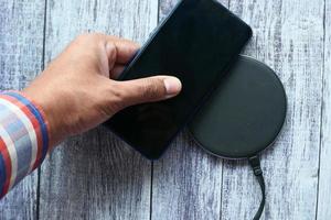 Man's hand charging a smartphone using wireless charging pad, top view
