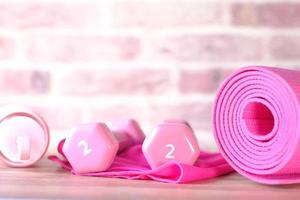 Pink colored dumbbells, exercise mat and water bottle on brick background photo