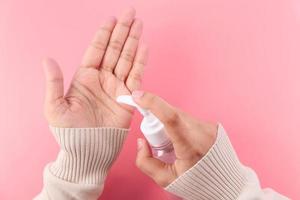 Young woman using hand sanitizer on pink background, top down view photo
