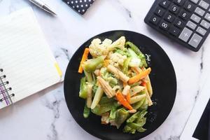 Concepto de alimentación saludable de verduras frescas cocidas en la placa en la mesa de la oficina foto