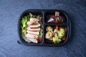 Sectioned plastic food container with sliced chicken salad, broccoli, carrots, and cabbage photo