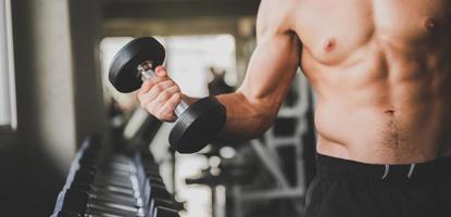 Hombre sujetando una pesa en un gimnasio con una fila de pesas en el fondo foto